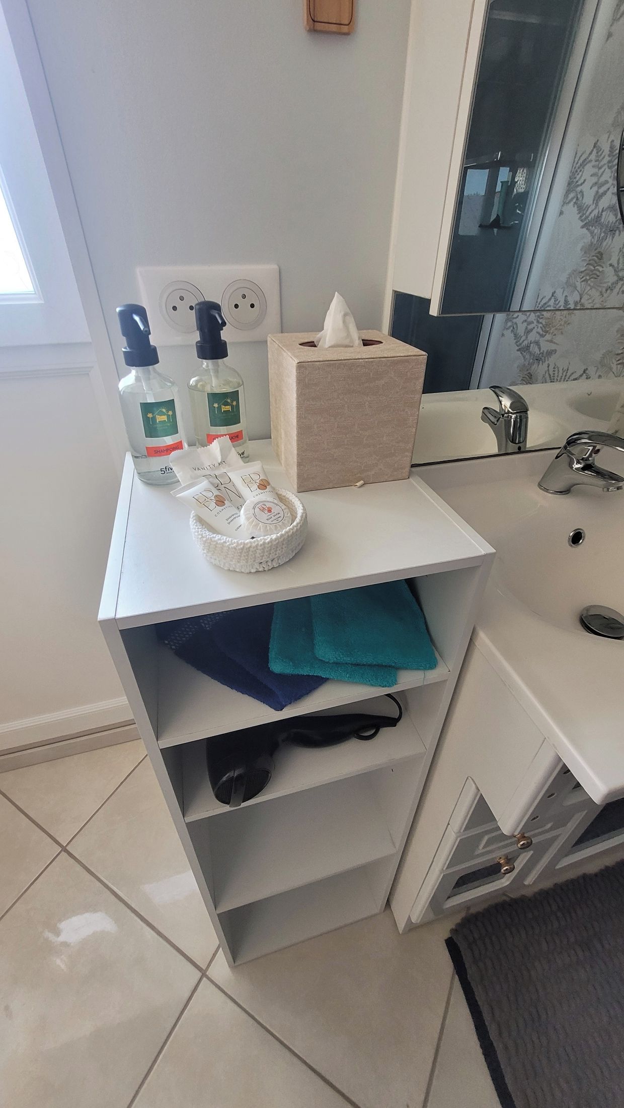 Een badkamer met een witte wastafel, een handdoekhouder, een zakdoos en toiletartikelen.