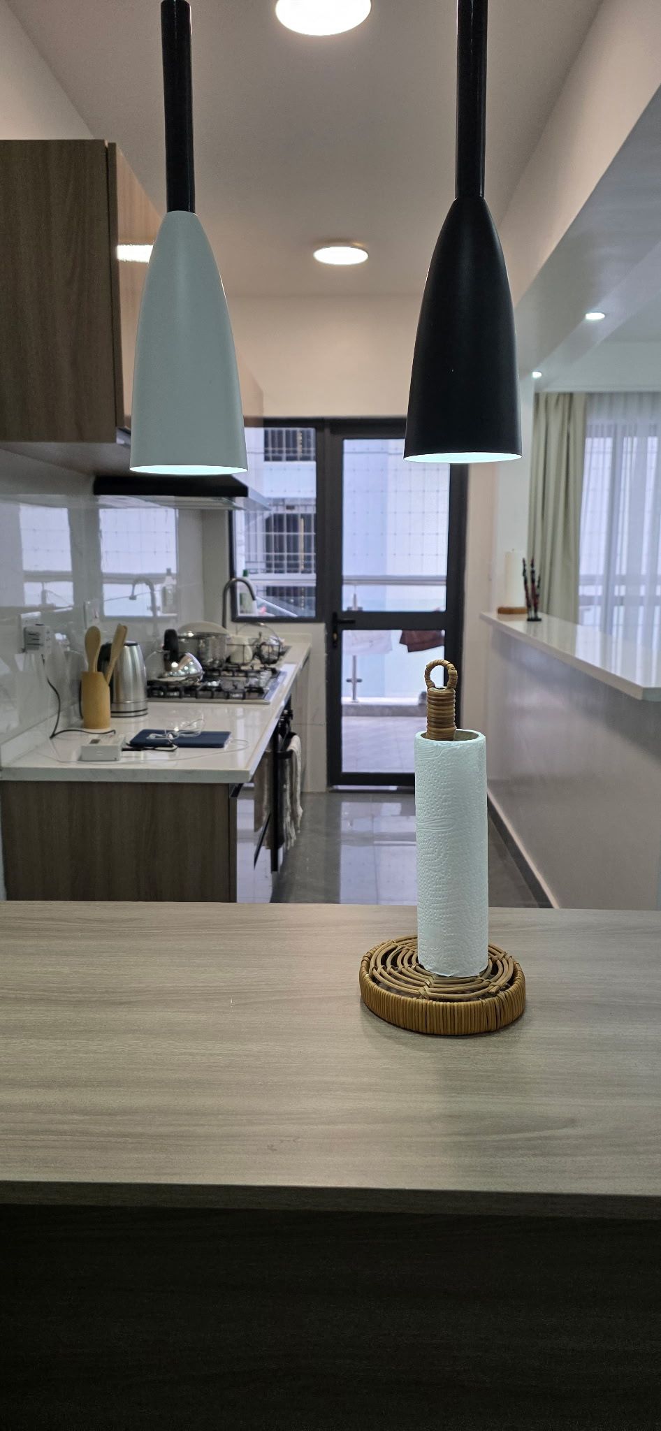 A modern kitchen with two pendant lights, a central island, and a view of the cityscape through large windows.