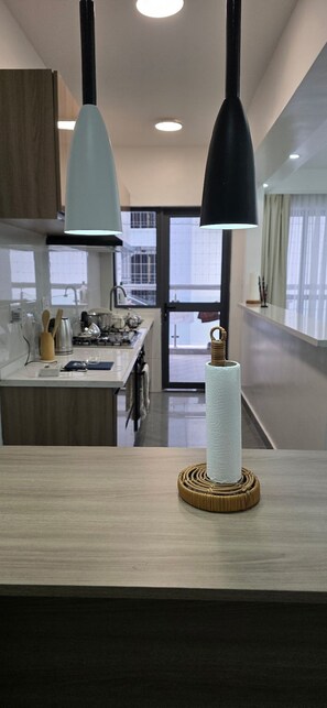 Eine moderne Küche mit zwei Pendelleuchten, einer zentralen Kochinsel und Blick auf die Stadt durch große Fenster.
