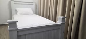 Un letto bianco con testiera, un cuscino bianco e tende beige.