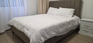 Un letto rifatto con un piumone bianco e cuscini, una testiera in legno e un comodino con cassetti.