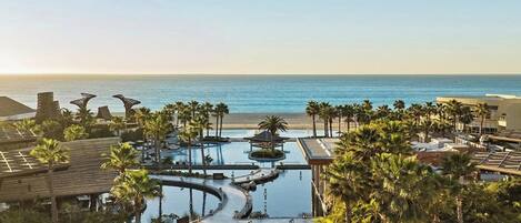 A resort with multiple swimming pools, palm trees, and a view of the ocean.