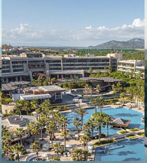 Un resort con varias piscinas, palmeras y un edificio grande con balcones.