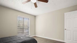 A bedroom with a bed, a ceiling fan, a window with blinds, and a white door.