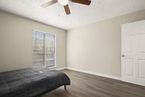 A bedroom with a bed, a ceiling fan, a window with blinds, and a white door.