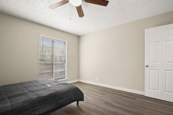 A bedroom with a bed, a ceiling fan, a window with blinds, and a white door.