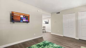 A hallway with a mounted TV, a green rug, and a door with a closet.