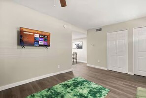 A hallway with a mounted TV, a green rug, and a door with a closet.