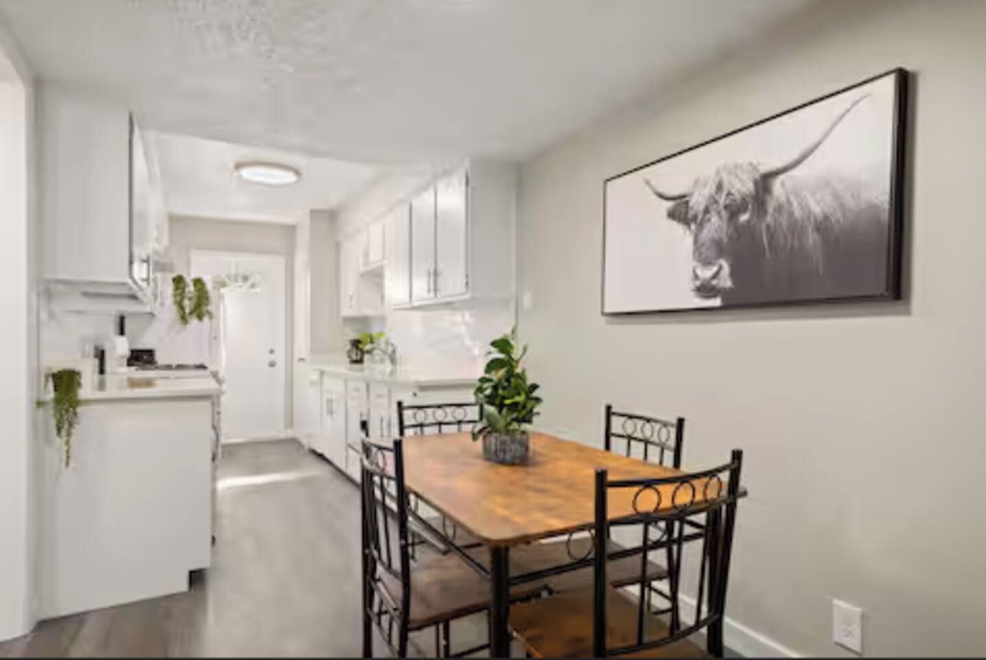 A modern kitchen with white cabinetry, a wooden dining table, and a black and white artwork on the wall.