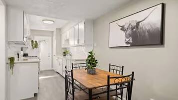 A modern kitchen with white cabinetry, a wooden dining table, and a black and white artwork on the wall.