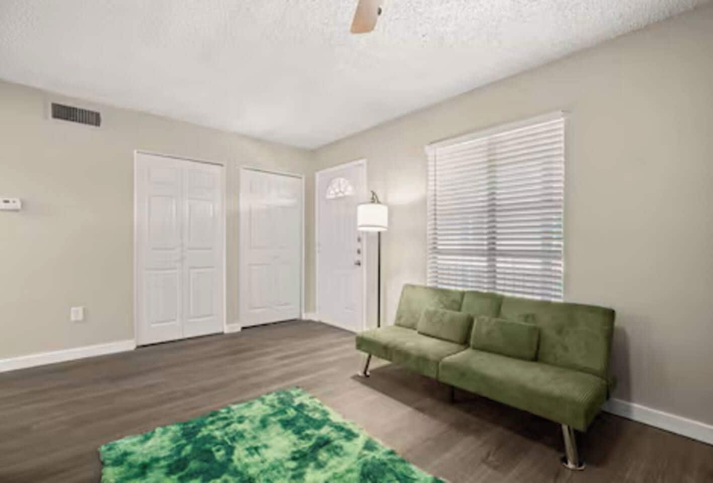 A room with a green couch, a patterned rug, and a ceiling fan.