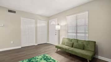 A room with a green couch, a patterned rug, and a ceiling fan.