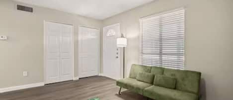 A room with a green couch, a patterned rug, and a ceiling fan.