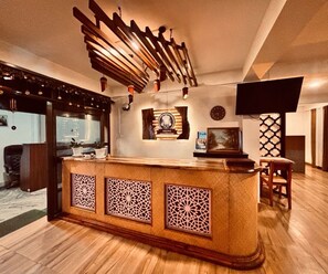 A reception area with a wooden counter, decorative wall panels, a clock, and a television mounted on the wall.