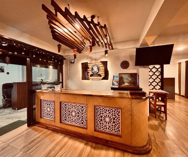A reception area with a wooden counter, decorative wall panels, a clock, and a television mounted on the wall.