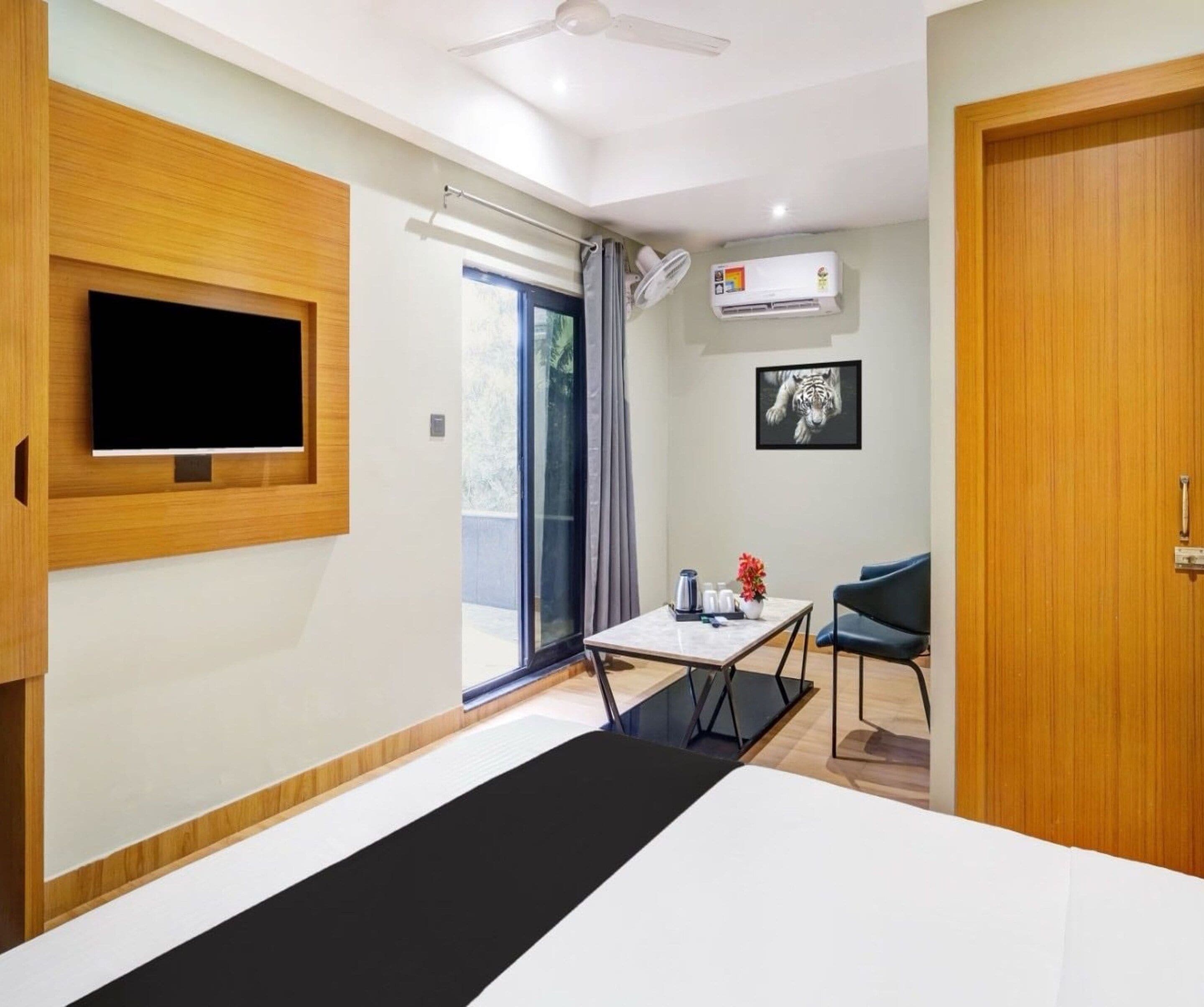 Una habitación de hotel con cama, televisión montada en la pared, una mesita con una silla, equipo de aire acondicionado y una puerta.