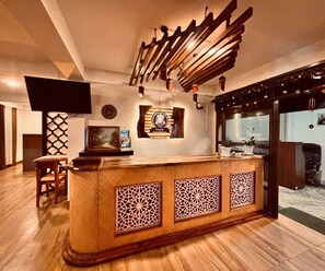 A reception area with a wooden counter, a clock, and a television mounted on the wall. - Deluxe Room Hotel Nirvis Grand (Guwahati)