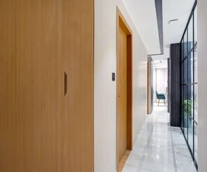 A modern hallway with a wooden door, a glass wall, and a chair. - Deluxe Room Hotel Nirvis Grand (Guwahati)