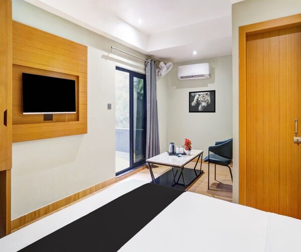 A modern hotel room with a bed, a flat-screen TV mounted on the wall, a small table with a chair, and a door.