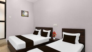 Een hotelkamer met twee bedden, een nachtkastje, een vaas met bloemen en een schilderij aan de muur.