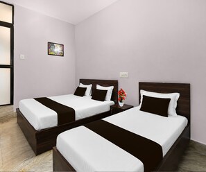 A hotel room with two beds, a nightstand, a vase with flowers, and a painting on the wall. - Deluxe Room Shree Ram Residency (Cuttack)