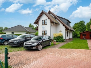 Ein zweistöckiges Haus mit Auffahrt, geparkten Autos und einem kleinen Schuppen.