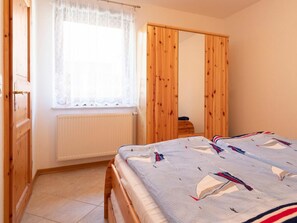 Ein Schlafzimmer mit einem Bett, einem Fenster mit Spitzenvorhängen, einem Holzschrank und einer Heizung.