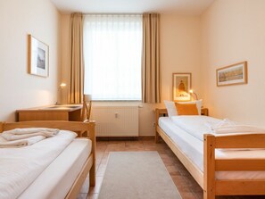 Ein Hotelzimmer mit zwei Einzelbetten, einem Schreibtisch, einem Stuhl, einem Heizkörper und einem Fenster mit Vorhängen.