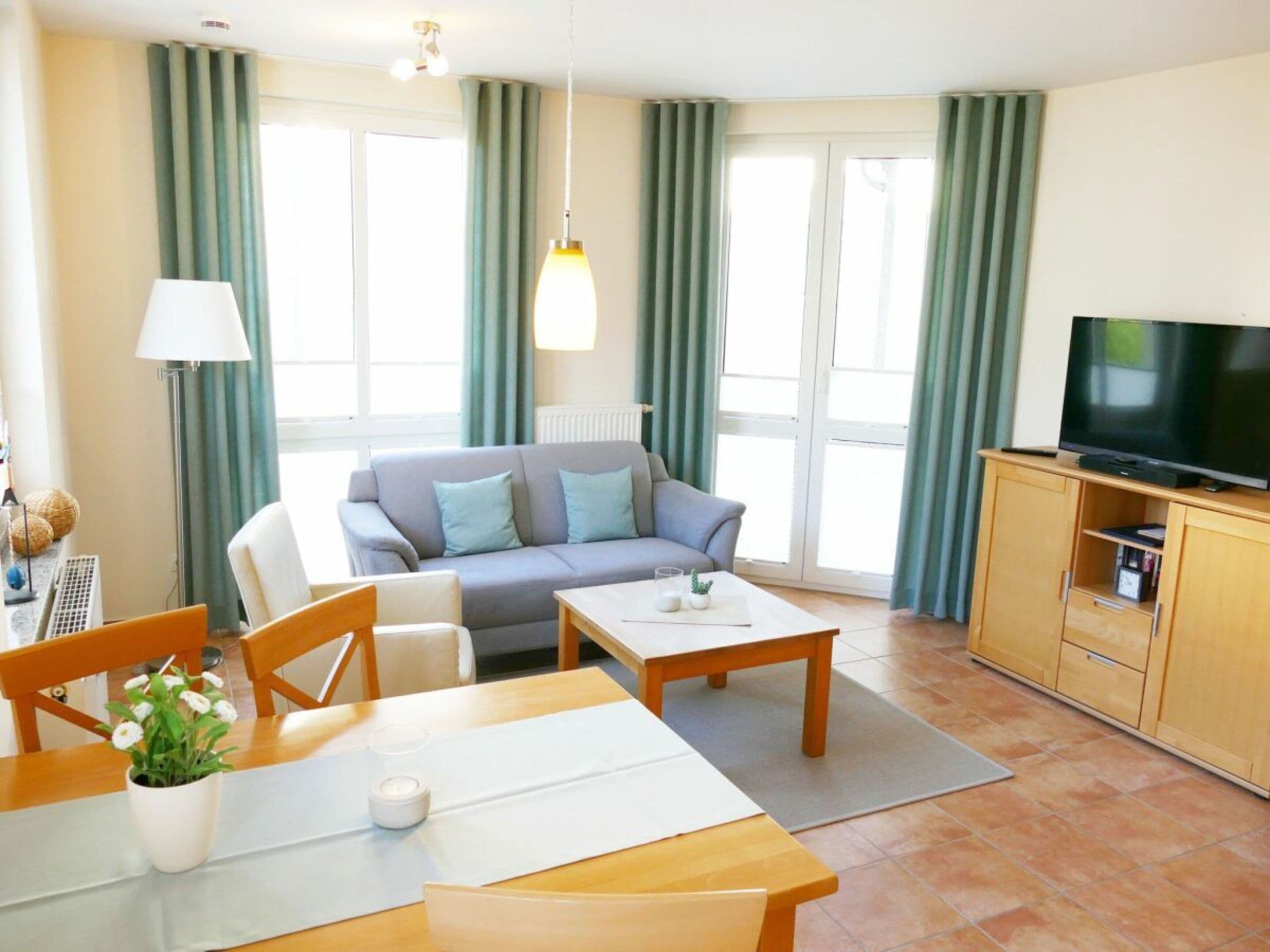 Una sala de estar moderna con sofá, mesa de centro, mesa de comedor y un televisor sobre un mueble de madera.