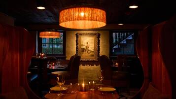 An interior with a dining table set for two, surrounded by chairs, under a large hanging lamp.