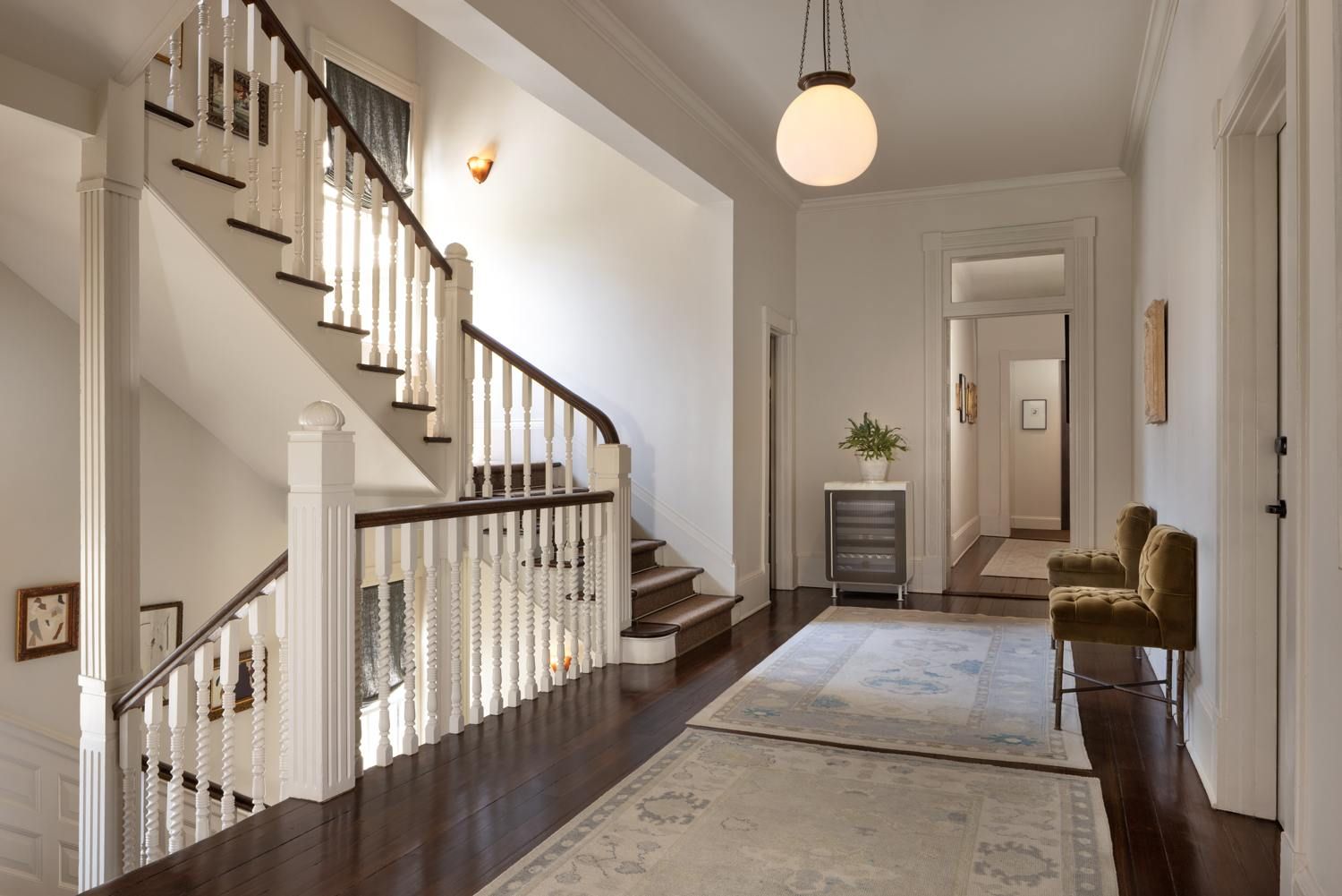 A spacious hallway with a wooden staircase, a hanging light fixture, and a rug.
