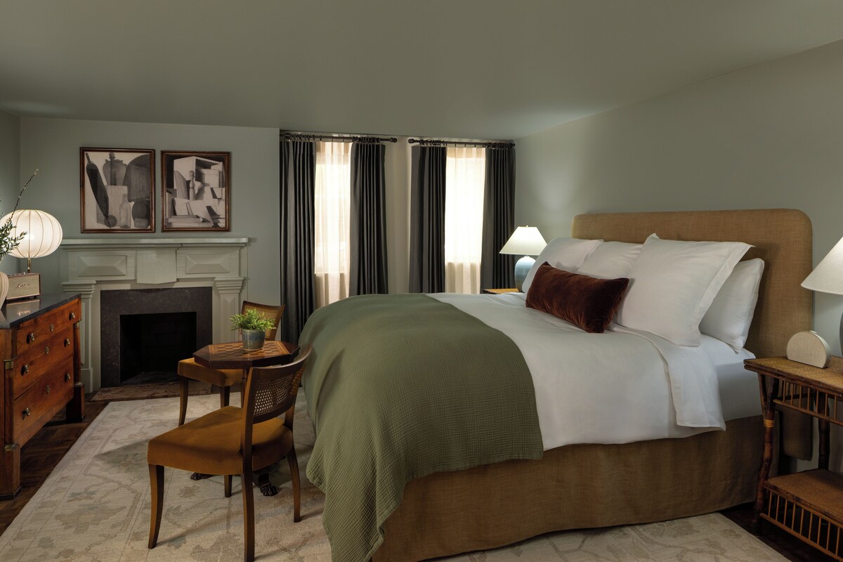 A bedroom with a large bed, a fireplace, a desk, and two lamps.
