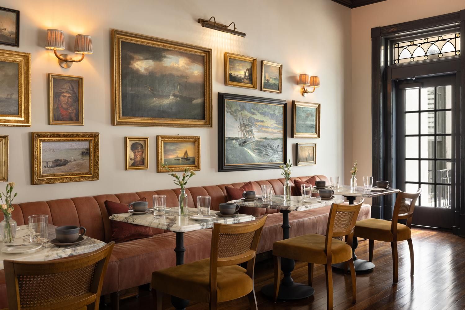 A restaurant with a long dining table set for multiple guests, cushioned seating, and wall-mounted artwork.