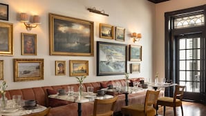 A restaurant with a long dining table set for multiple guests, cushioned seating, and wall-mounted artwork. - The Douglas Hotel Savannah (Savannah)