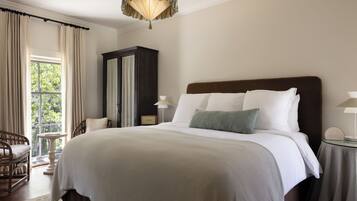 A hotel room with a large bed, a wooden wardrobe, a sitting area with a chair, and a view through a window.