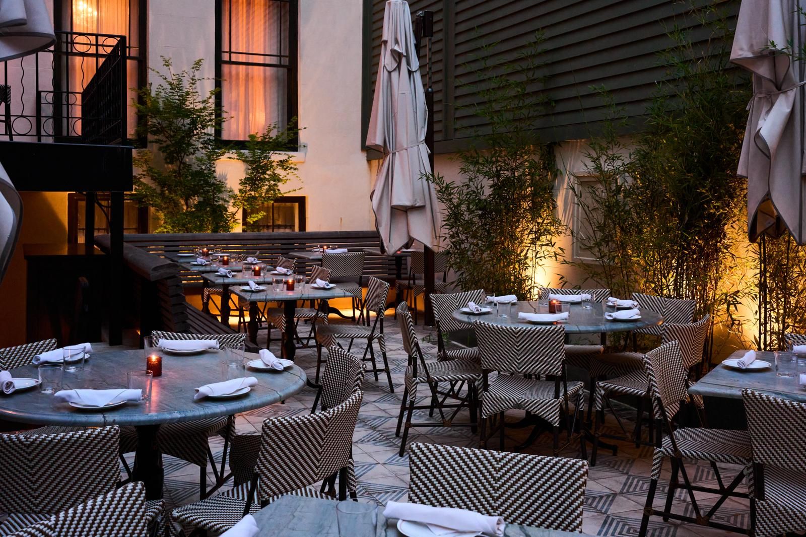 An outdoor dining area with multiple tables and chairs, some with umbrellas.