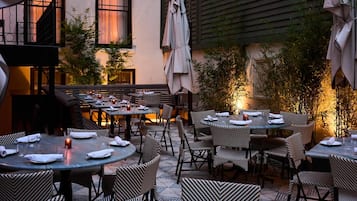 An outdoor dining area with multiple tables and chairs, some with umbrellas.