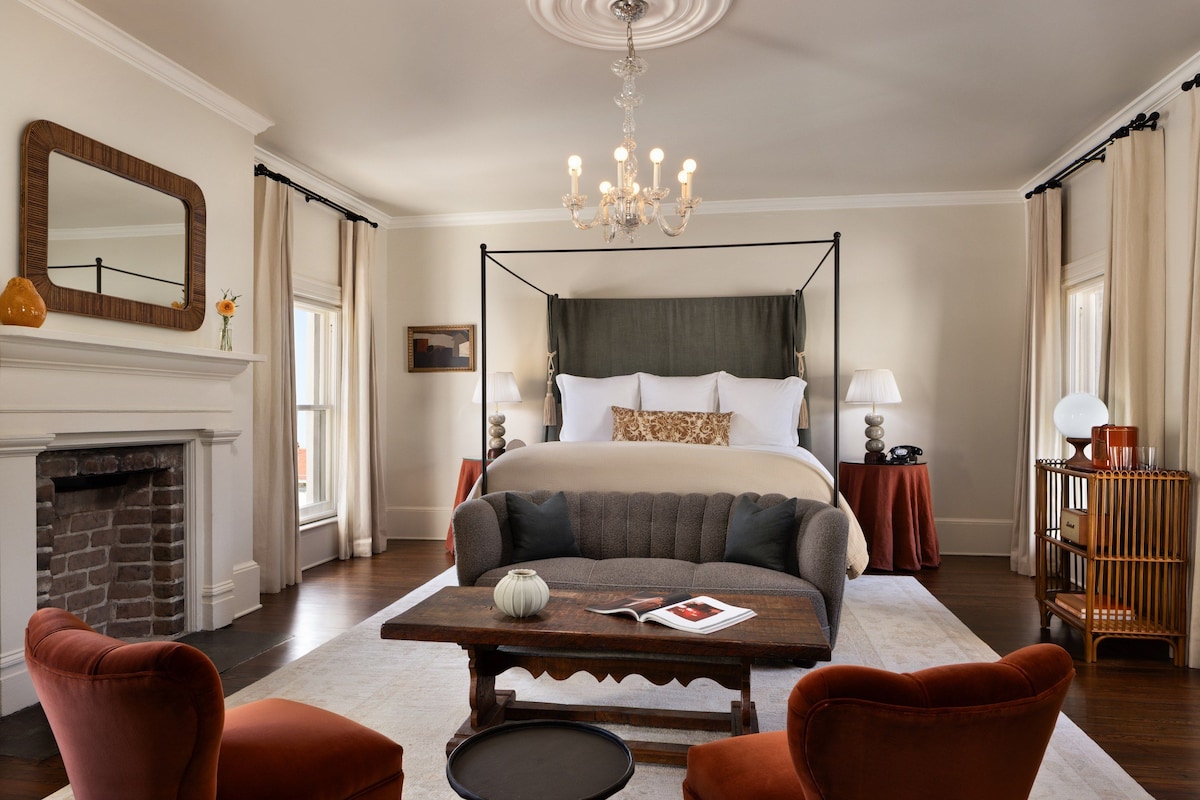 Un dormitorio con cama con dosel, candelabro, chimenea y una mesa de centro.