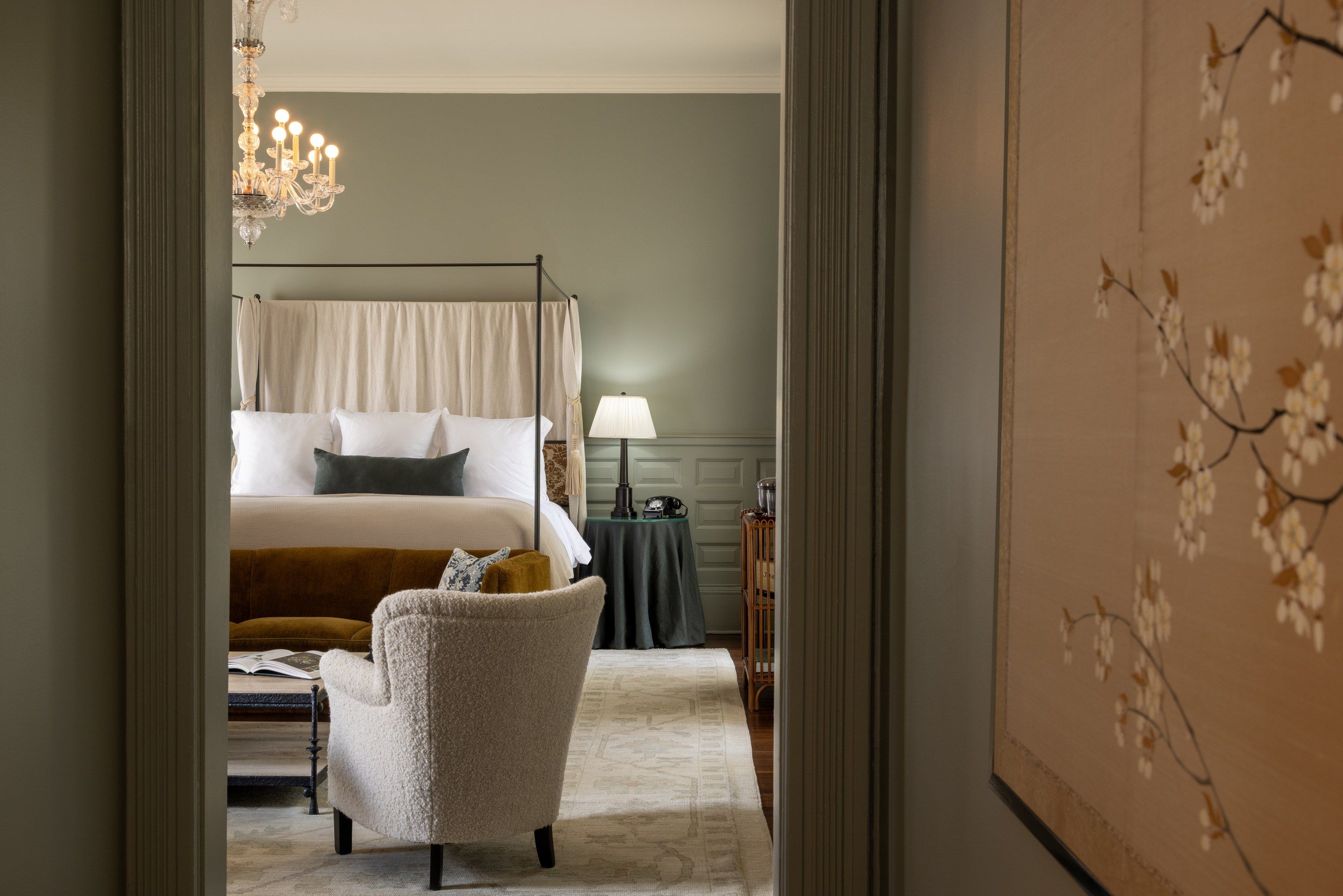 A bedroom with a four-poster bed, a side table with a lamp, and a chair.