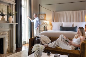 Una habitación de hotel con cama, sofá, chimenea y un ventanal grande.