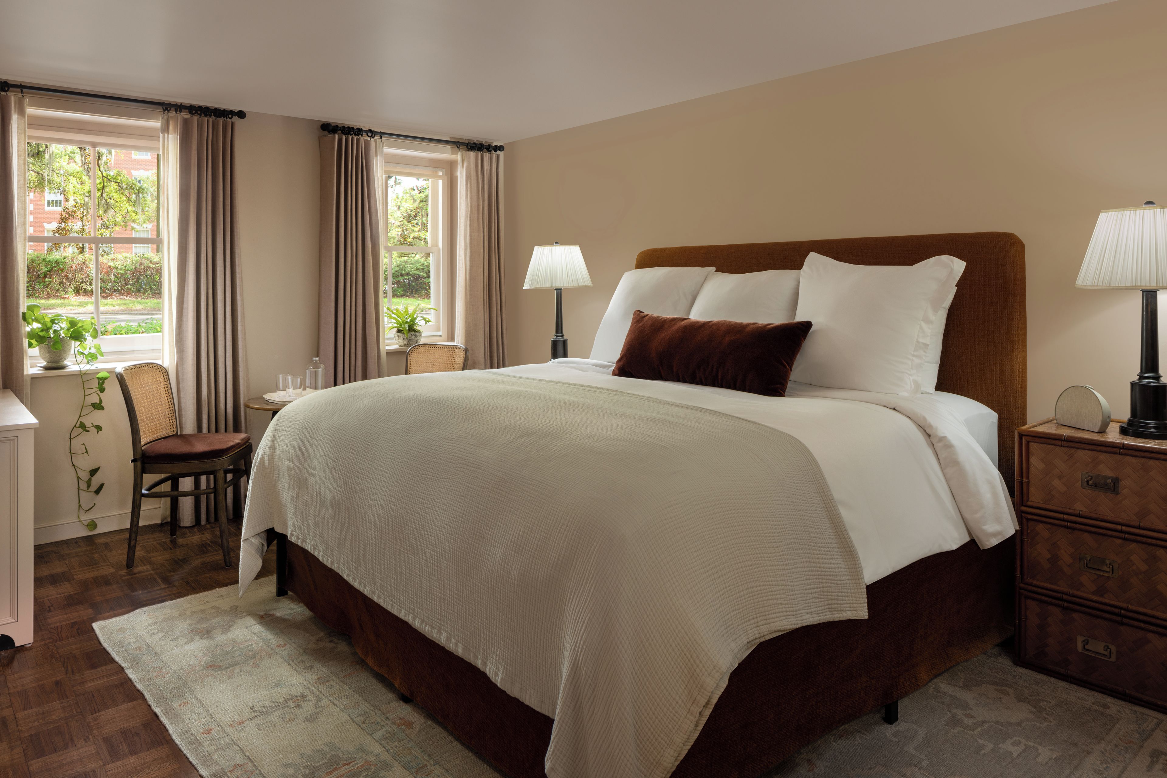 A hotel room with a large bed, a bedside table, a chair, a desk, and a view of the outdoors through the window.