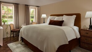 A hotel room with a large bed, bedside lamps, a chair, a small table, and a window with curtains. - The Douglas Hotel Savannah (Savannah)
