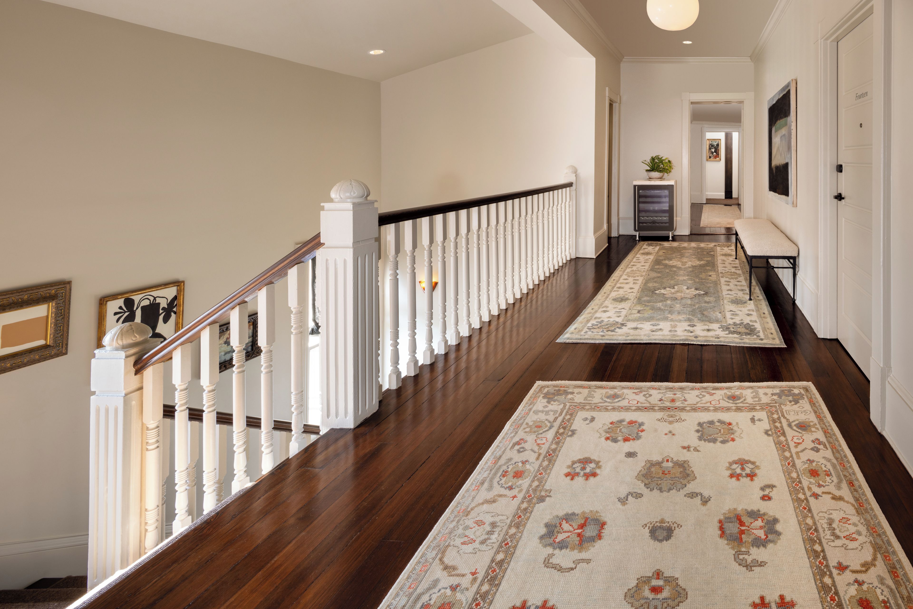 A hallway with a wooden floor, white railing, and patterned rugs.