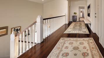 A hallway with a wooden floor, white railing, and patterned rugs.