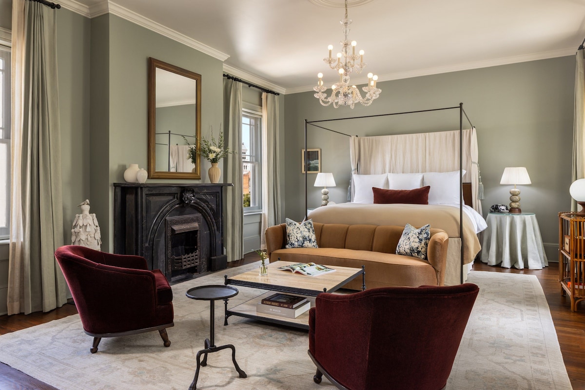 Un dormitorio con cama con dosel, candelabro, chimenea y vistas al exterior.