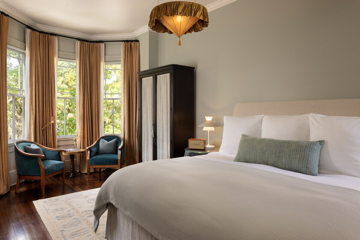 Habitación de hotel con una cama grande, un escritorio con silla, un armario y una ventana con cortinas.