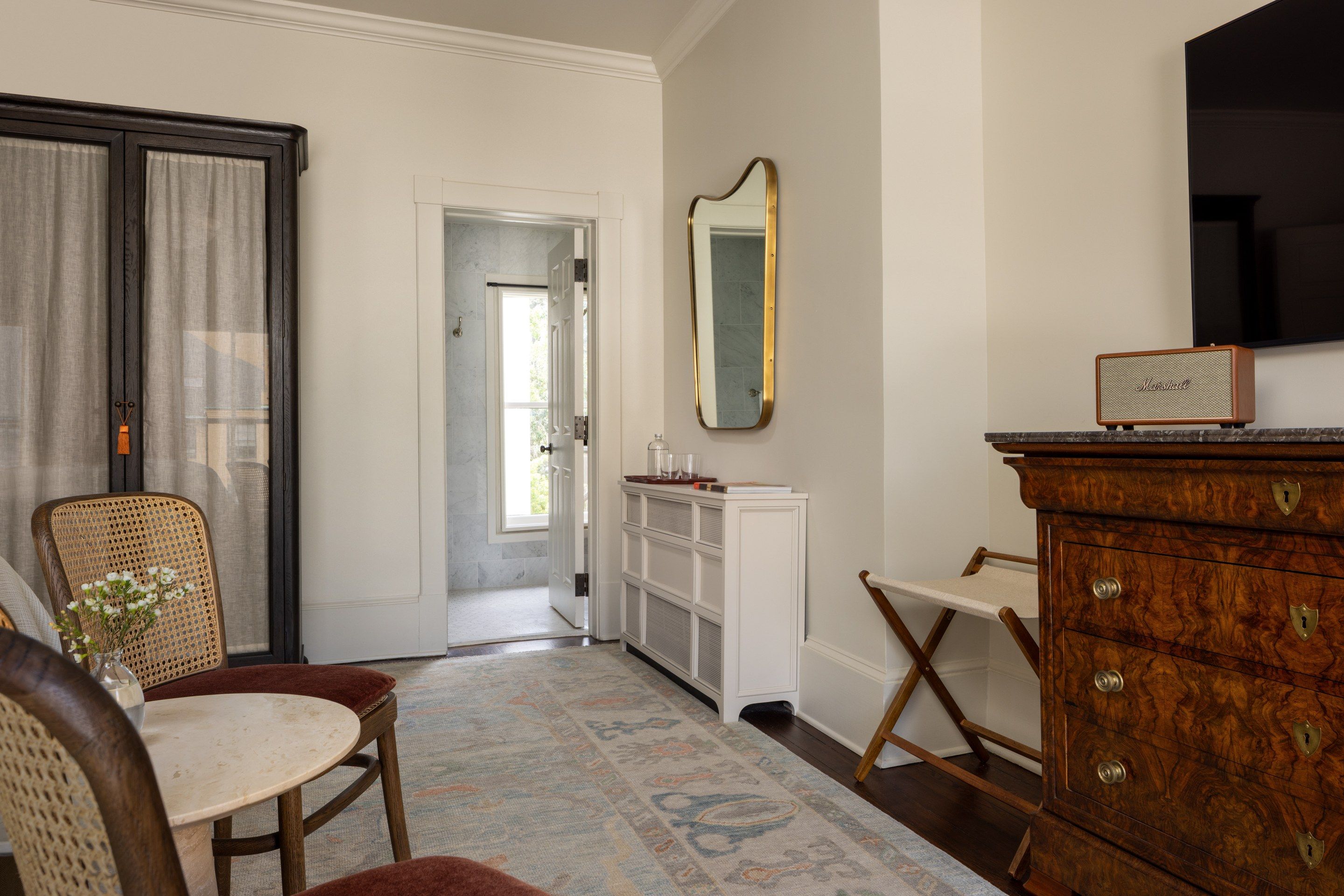 A bathroom with a wooden vanity, a mirror, a white cabinet, and a chair.