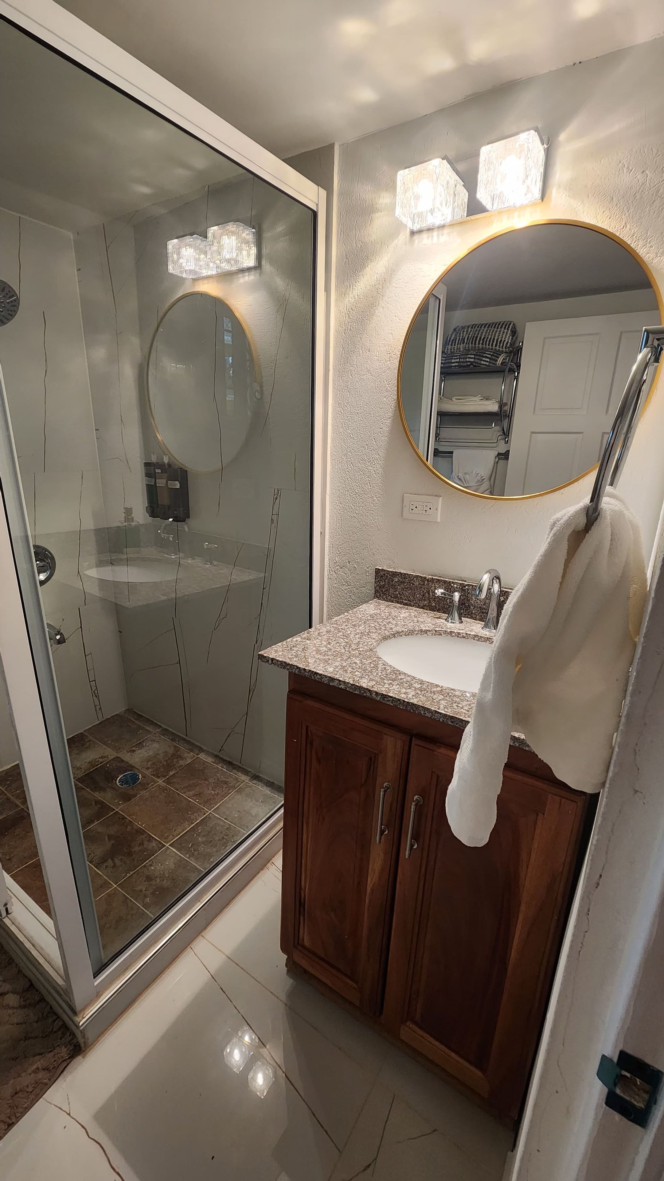 Une salle de bain dotée d’une douche à parois de verre, d’un meuble-lavabo avec un plan de travail en granit et d’un miroir avec un cadre doré.