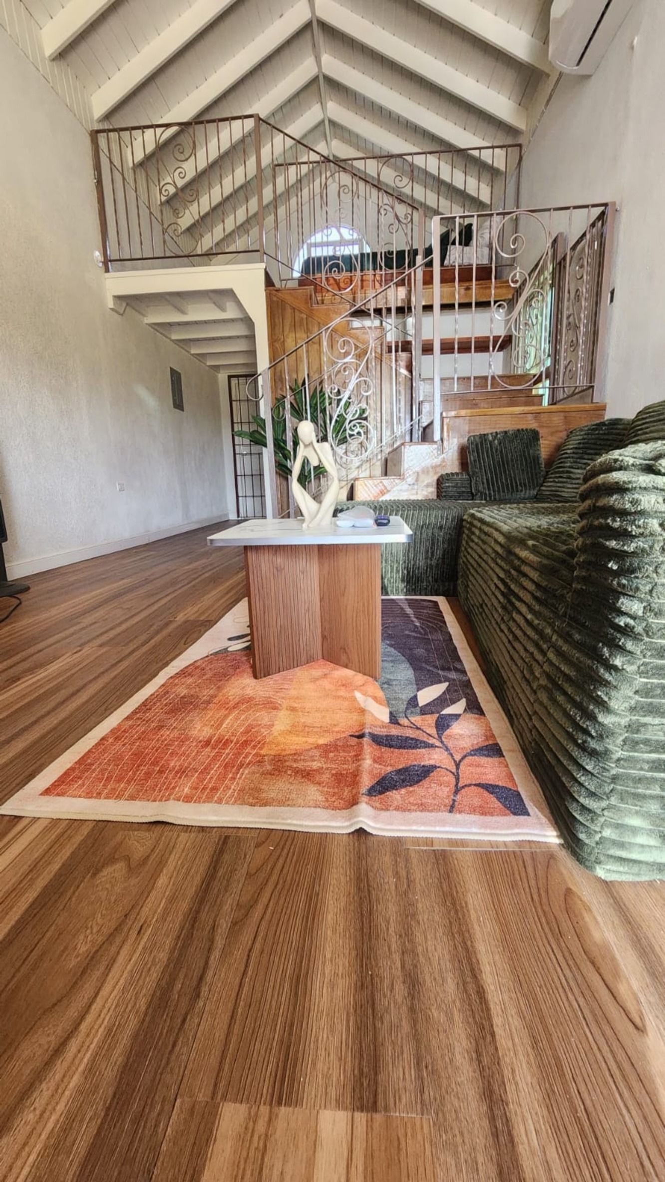 Une pièce spacieuse avec un plancher en bois, une table centrale et un grand tapis vert.