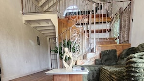 Quarto amplo com piso de madeira, uma mesa central e um tapete grande de cor verde.